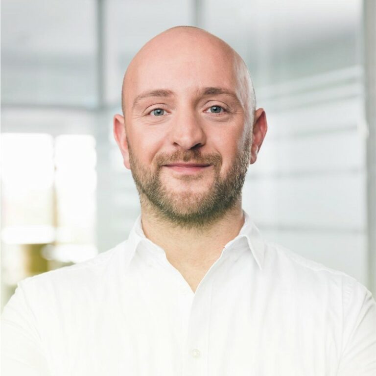 Professional headshot of a smiling bald man with a beard.