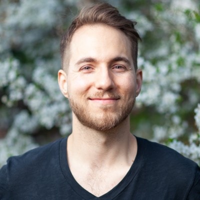A man with a beard smiling against flowering tree background.