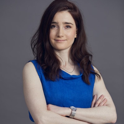 Woman in a blue sleeveless dress with arms crossed.