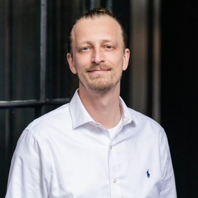 Smiling man with a bun wearing a white shirt.