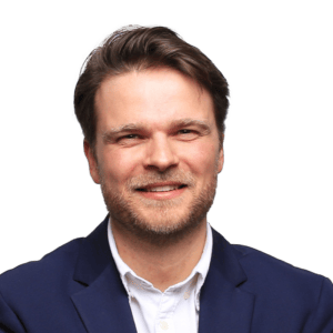 Smiling man with brown hair and beard in blue blazer.