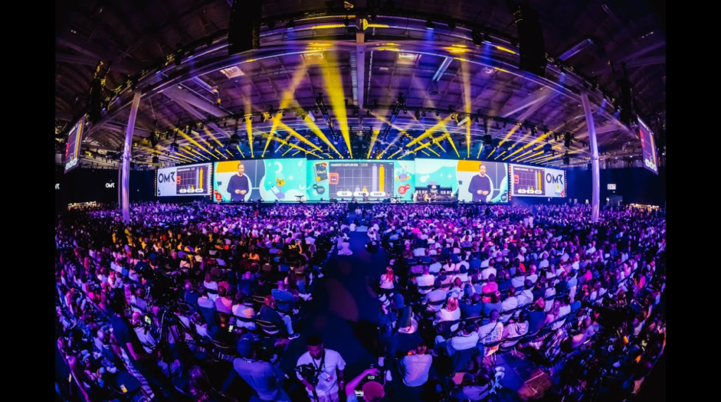 Crowded OMR conference hall with a massive stage and audience
