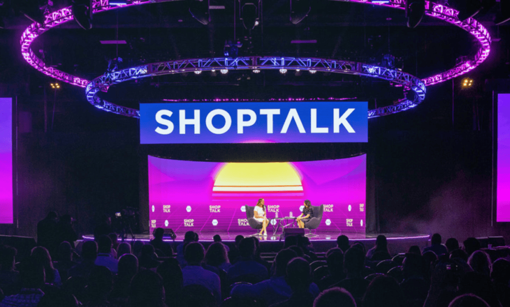 Two speakers on a neon-lit Shoptalk stage with audience.