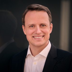 Professional headshot of a smiling man in a blazer.