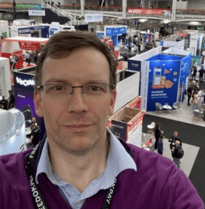 Man taking a selfie at a crowded exhibition hall.