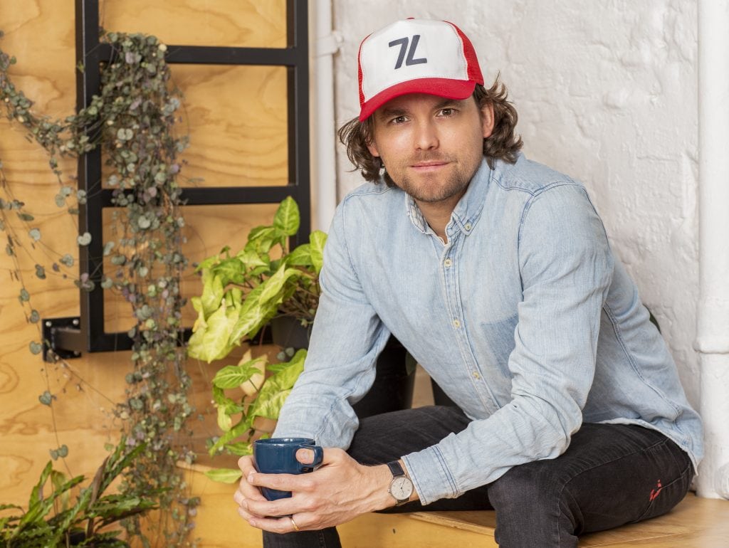 Man in denim shirt and trucker hat holding blue mug.