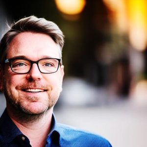 Smiling man with glasses in a blue shirt.