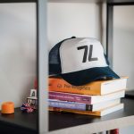 A trucker hat with '7L' logo atop stacked books.