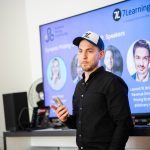 A presenter stands in front of a 7Learnings speaker screen.