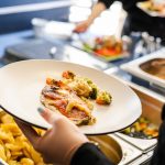 Hand holding a white plate with food at a buffet.