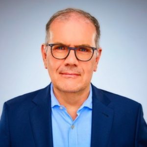 Professional headshot of a man with glasses in a suit.
