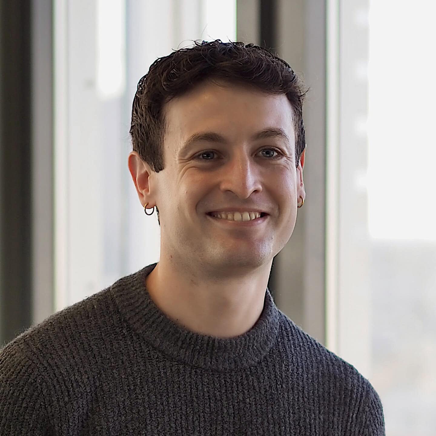 Headshot of a smiling young man in a gray sweater