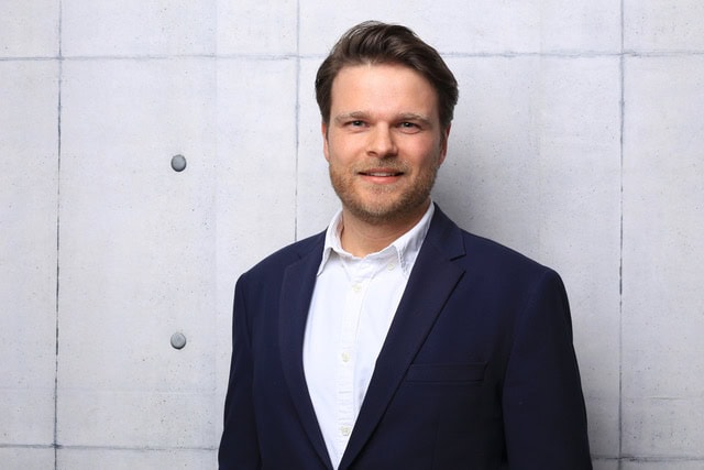 Professional headshot of a smiling man in a navy blazer.