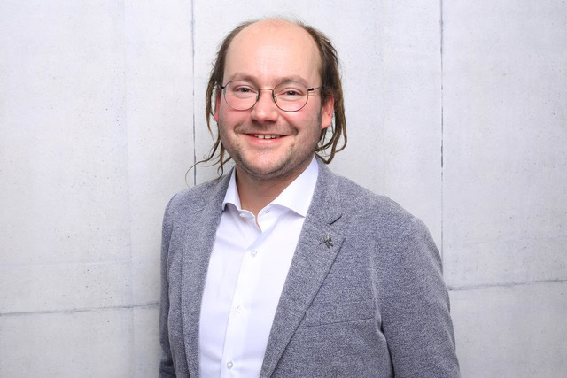 Professional portrait of a smiling man wearing glasses.