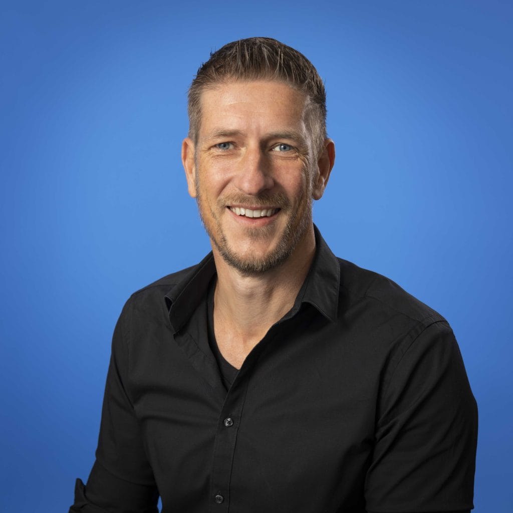 Smiling man in a black shirt on blue background.