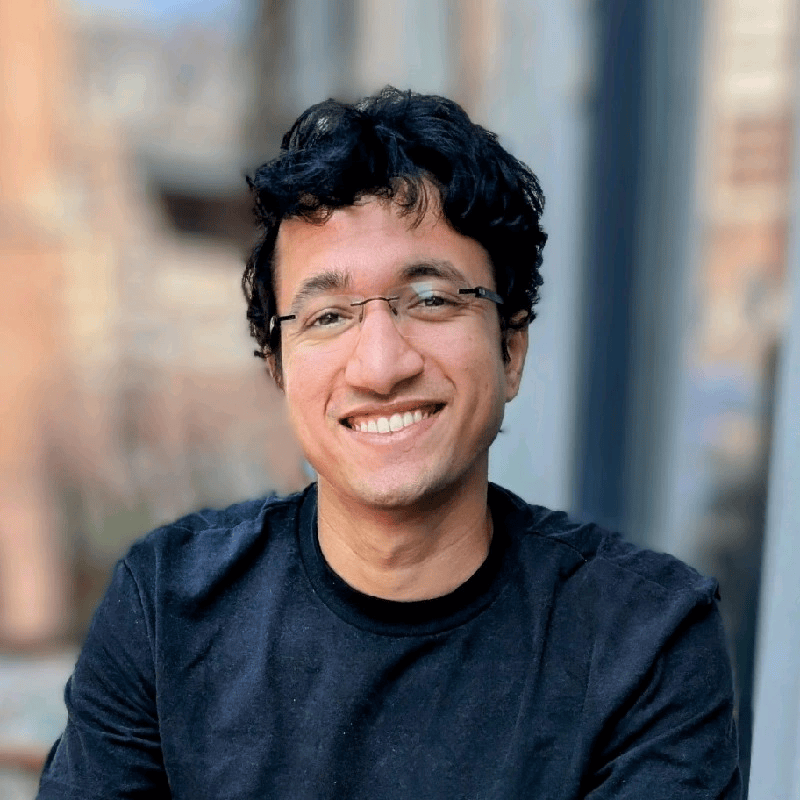 A smiling young man with dark curly hair and glasses.