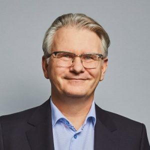 Professional headshot of a smiling man with glasses and suit.