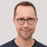 Headshot of a smiling man wearing glasses and blue shirt.