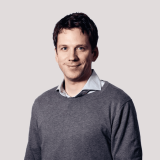 Smiling man with dark hair wearing a grey sweater