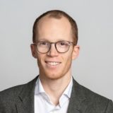 Professional headshot of a man with glasses and a blazer.