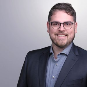 Smiling man with beard and glasses in a professional suit.